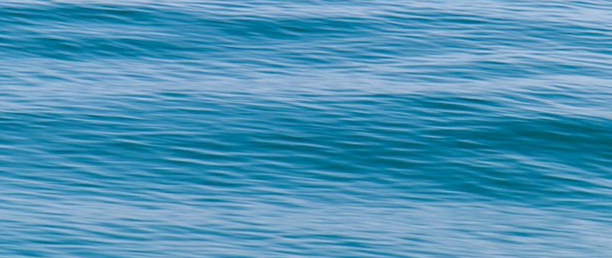 a ripple of ocean Blonde-haired woman relaxes on a cliff, looking out at the Pacific Ocean on a beautiful day. She is wearing a light colored t-shirt with an army green cardigan and light jeans.