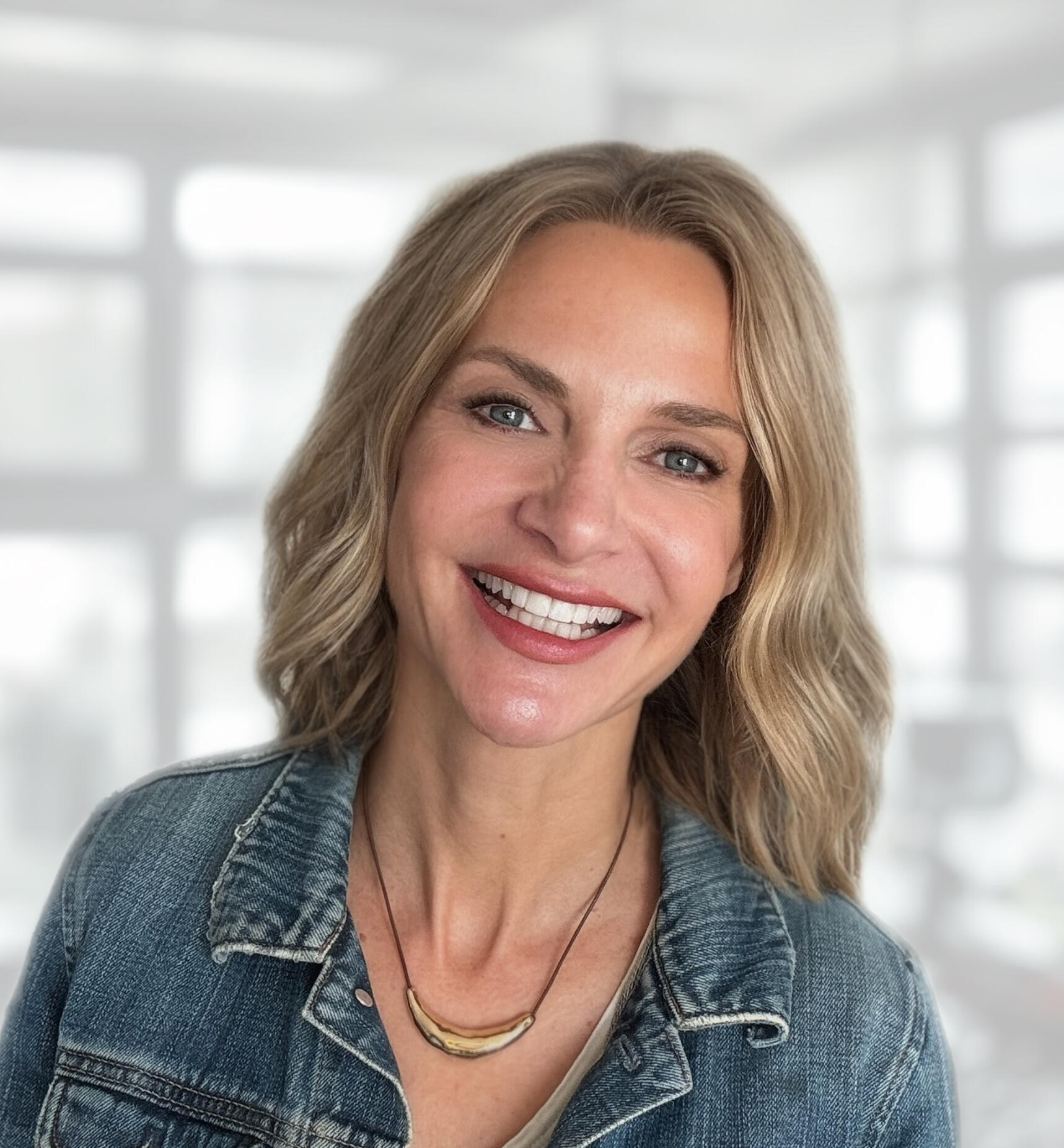 MIchelle (Mika) Waters, Founder of Waters Edge Co Close-up headshot of blonde-haired woman smiling for the camera. She is wearing a light colored denim jacket.